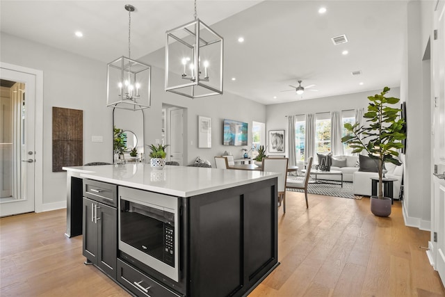 kitchen featuring stainless steel microwave, pendant lighting, a kitchen island, light wood-type flooring, and ceiling fan