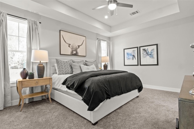 bedroom featuring ceiling fan, multiple windows, a raised ceiling, and carpet flooring