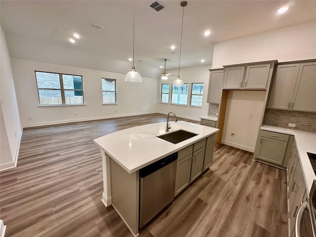 kitchen featuring decorative light fixtures, an island with sink, sink, backsplash, and stainless steel dishwasher