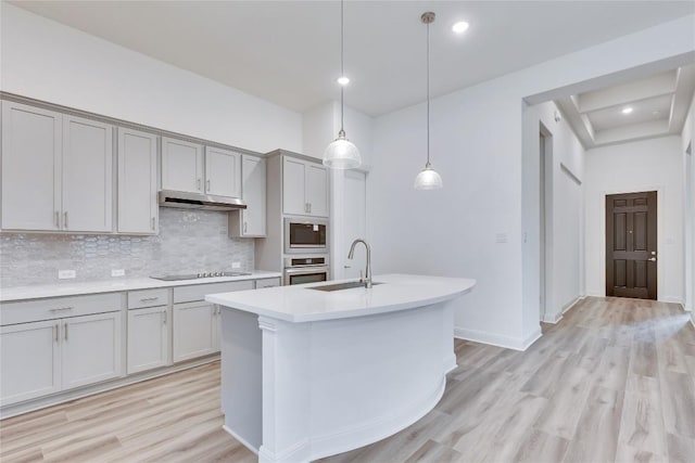 kitchen with under cabinet range hood, a sink, light countertops, appliances with stainless steel finishes, and gray cabinets