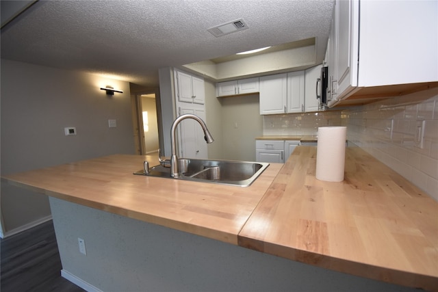 kitchen with sink, backsplash, wood counters, kitchen peninsula, and white cabinetry