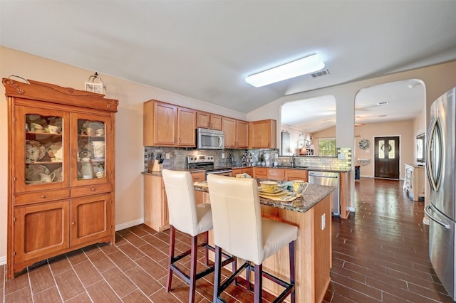 kitchen with appliances with stainless steel finishes, kitchen peninsula, vaulted ceiling, decorative backsplash, and a breakfast bar area