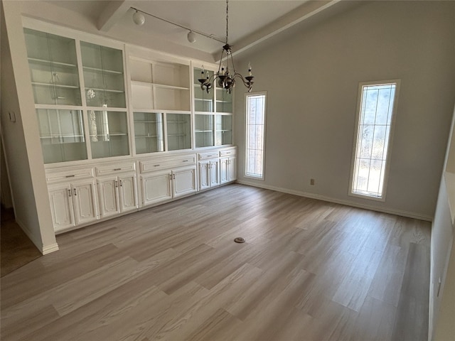 unfurnished dining area featuring lofted ceiling with beams, a notable chandelier, rail lighting, and light wood-type flooring