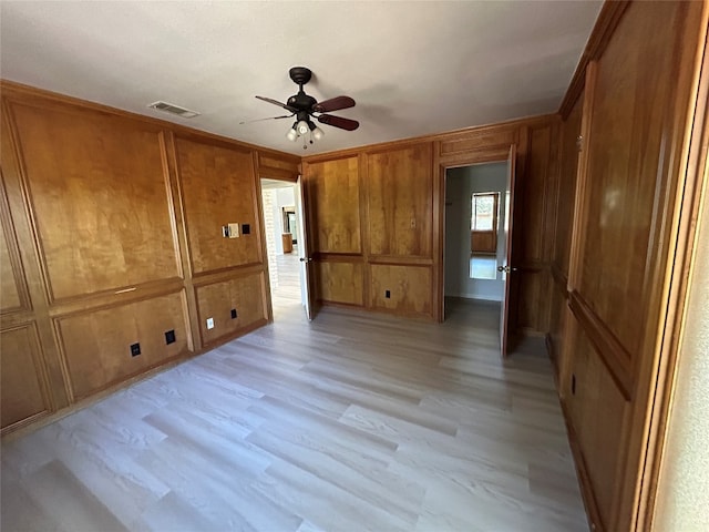 unfurnished bedroom with wood walls, light wood-type flooring, and ceiling fan