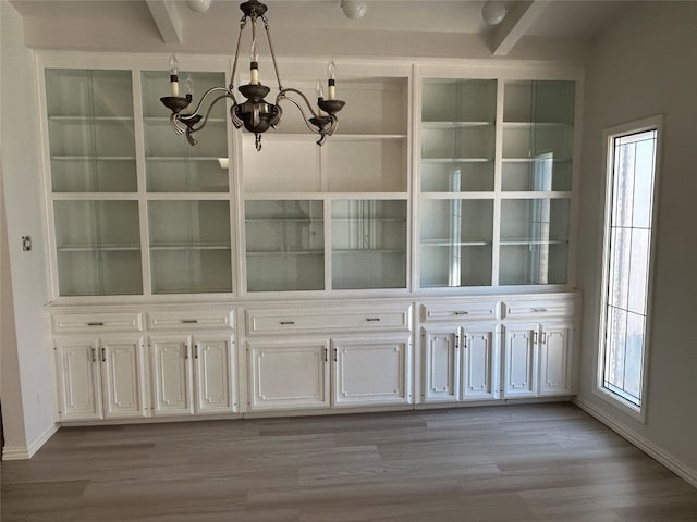 unfurnished dining area featuring a notable chandelier, beam ceiling, and light wood-type flooring