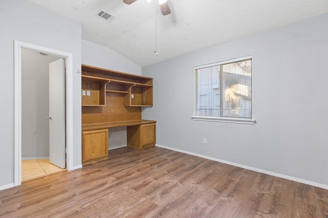 unfurnished office featuring built in desk, lofted ceiling, light hardwood / wood-style floors, and ceiling fan