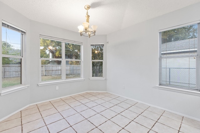 tiled spare room with an inviting chandelier, a textured ceiling, and a healthy amount of sunlight