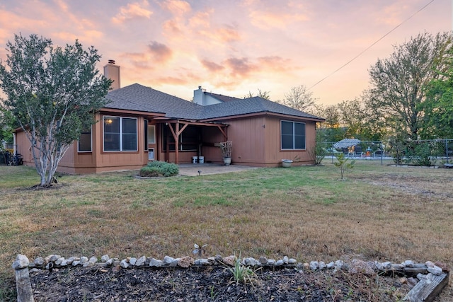 back house at dusk featuring a lawn