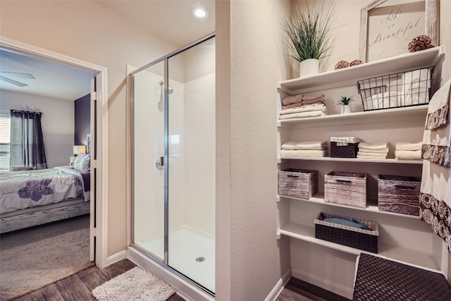 bathroom with hardwood / wood-style flooring, a shower with shower door, and ceiling fan