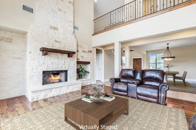 living room with a stone fireplace, a towering ceiling, and hardwood / wood-style flooring