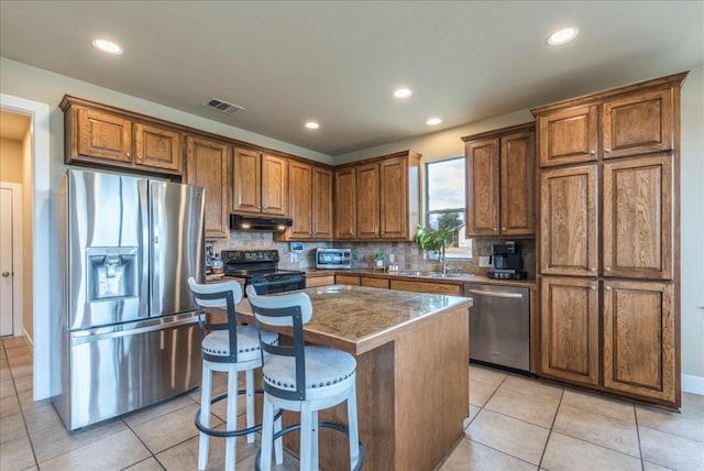 kitchen with appliances with stainless steel finishes, backsplash, a kitchen breakfast bar, sink, and a kitchen island