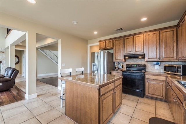 kitchen featuring decorative backsplash, a breakfast bar, stainless steel appliances, a center island, and light tile patterned flooring