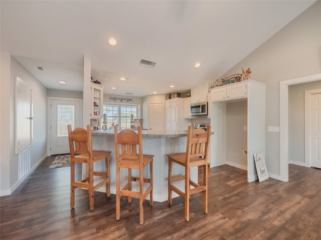 kitchen featuring kitchen peninsula, white cabinetry, vaulted ceiling, dark wood-type flooring, and light stone counters