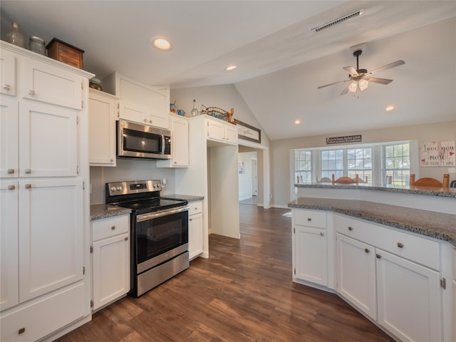 kitchen with dark wood-type flooring, dark stone counters, vaulted ceiling, white cabinetry, and appliances with stainless steel finishes