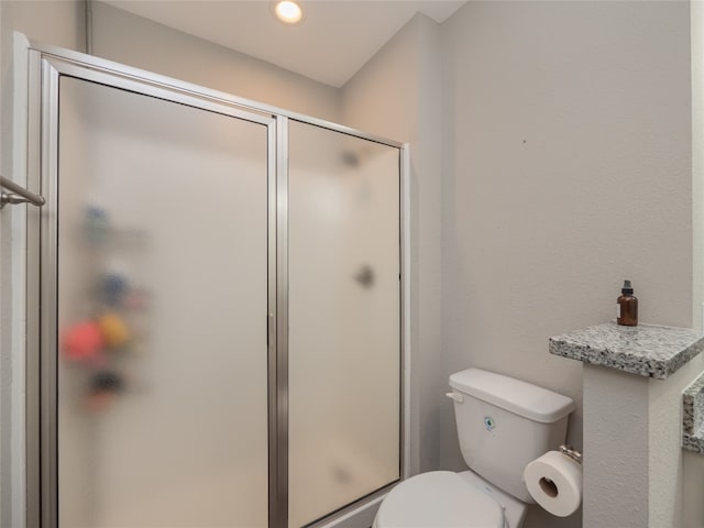 bathroom featuring a shower with door and toilet