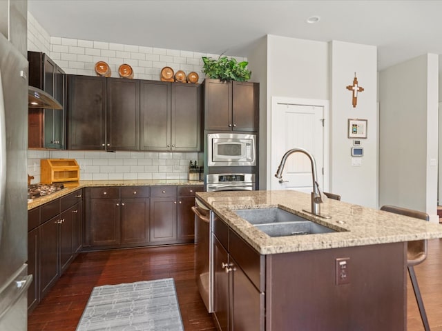 kitchen featuring dark hardwood / wood-style flooring, appliances with stainless steel finishes, a kitchen island with sink, light stone countertops, and sink