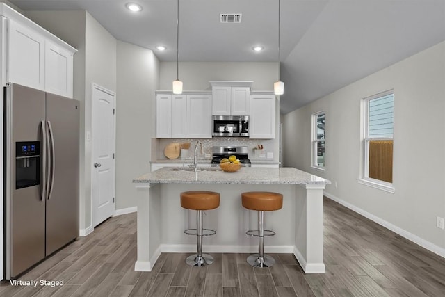 kitchen featuring stainless steel appliances, hanging light fixtures, a center island with sink, and white cabinets