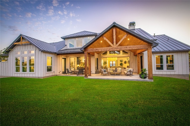 back house at dusk with an outdoor living space, a patio area, and a lawn