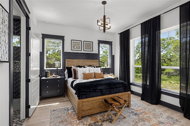 bedroom with light hardwood / wood-style floors, multiple windows, and an inviting chandelier