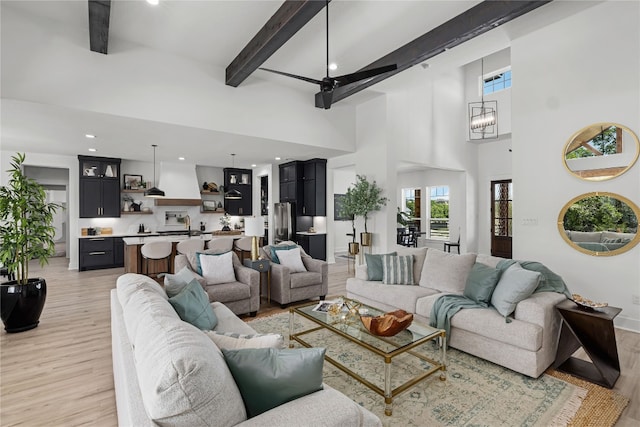 living room featuring beam ceiling, an inviting chandelier, a high ceiling, and light hardwood / wood-style floors