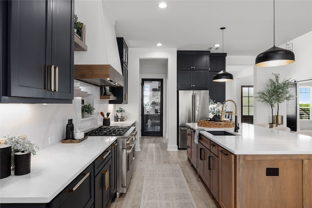 kitchen with a kitchen island with sink, high quality appliances, sink, pendant lighting, and light wood-type flooring