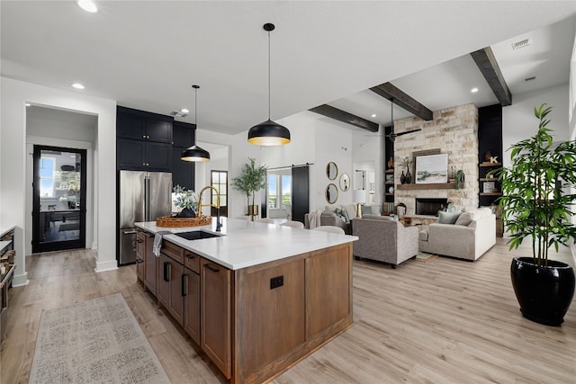 kitchen with sink, light wood-type flooring, a barn door, hanging light fixtures, and a kitchen island with sink