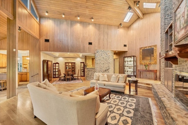 living room with light hardwood / wood-style floors, high vaulted ceiling, wooden ceiling, and a stone fireplace