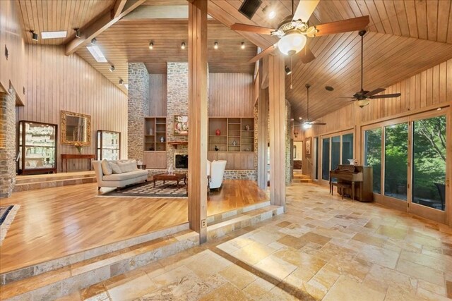 100 Silver Spur, Horseshoe Bay, TX 78657 - unfurnished living room featuring high vaulted ceiling, a stone fireplace, a ceiling fan, stone tile floors, and wood ceiling with exposed beams