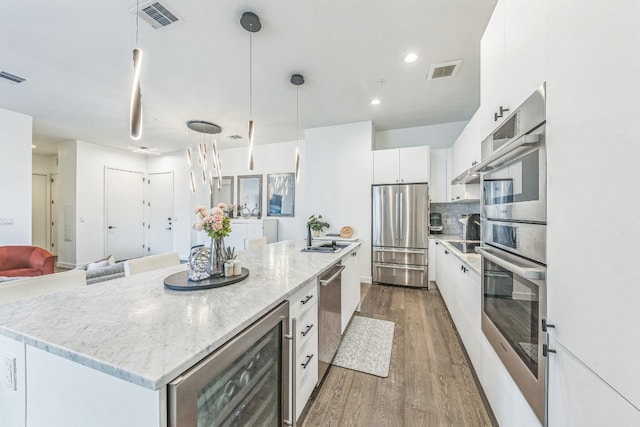 kitchen featuring a kitchen island, stainless steel appliances, hardwood / wood-style floors, decorative light fixtures, and white cabinetry