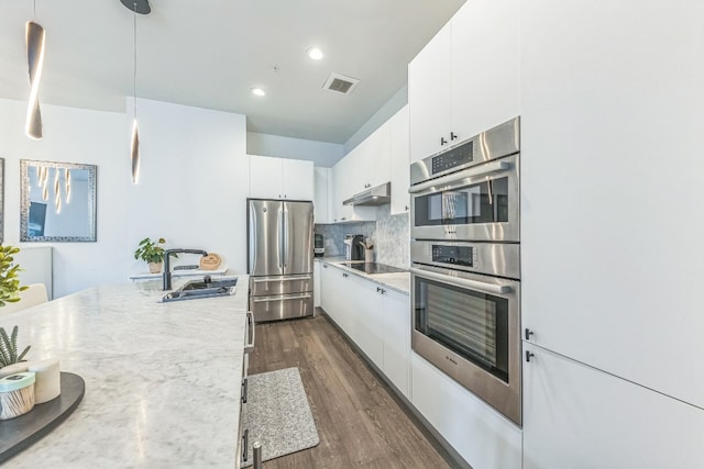 kitchen with appliances with stainless steel finishes, sink, hanging light fixtures, white cabinets, and dark wood-type flooring