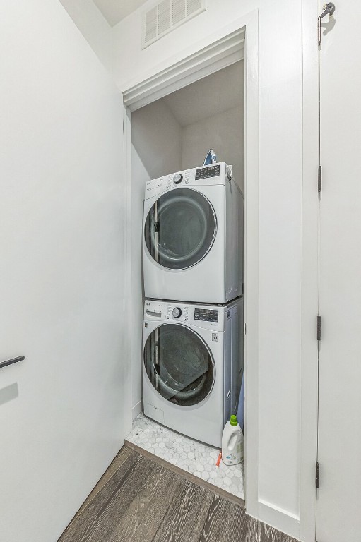 laundry area with stacked washer and dryer and dark hardwood / wood-style flooring