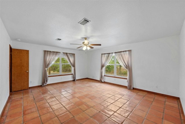 empty room with ceiling fan, a textured ceiling, light tile patterned flooring, and plenty of natural light