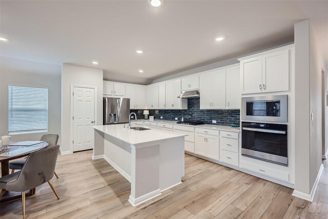 kitchen with white cabinets, stainless steel appliances, light hardwood / wood-style flooring, and a kitchen island with sink