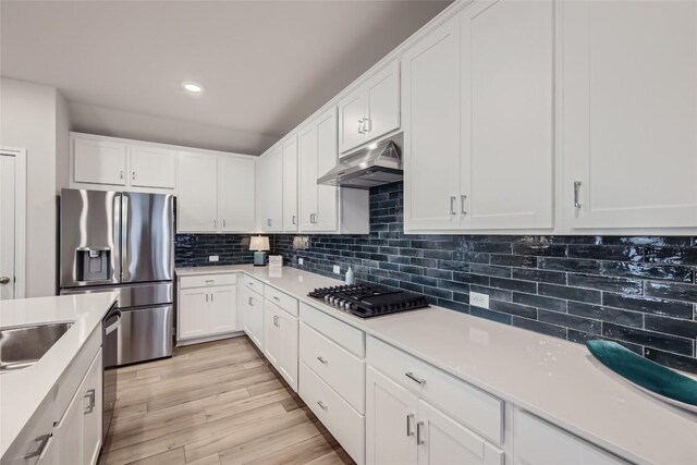 kitchen featuring sink, light hardwood / wood-style floors, decorative backsplash, white cabinets, and appliances with stainless steel finishes