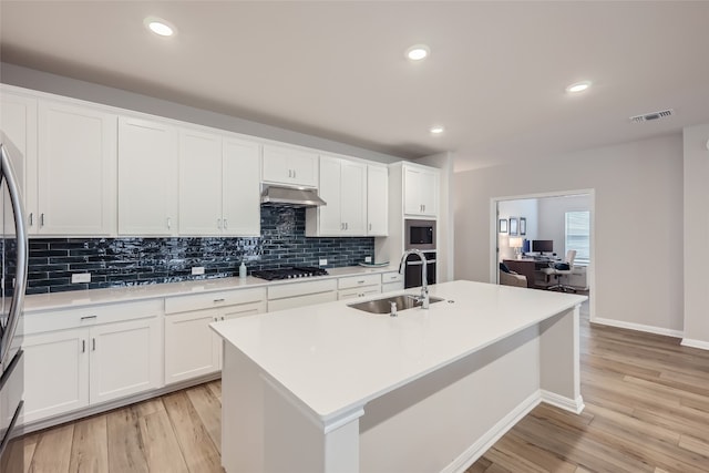 kitchen featuring sink, light hardwood / wood-style floors, white cabinetry, stainless steel microwave, and an island with sink