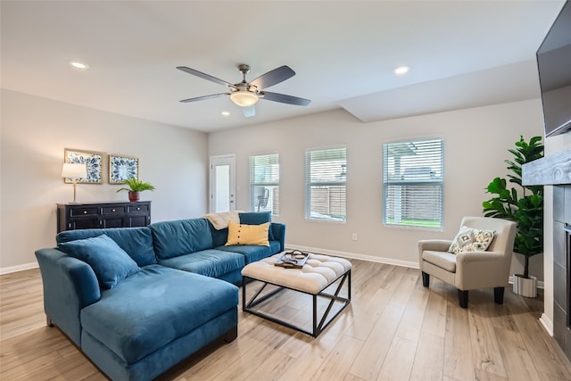 living room featuring light wood-type flooring, ceiling fan, and a tiled fireplace