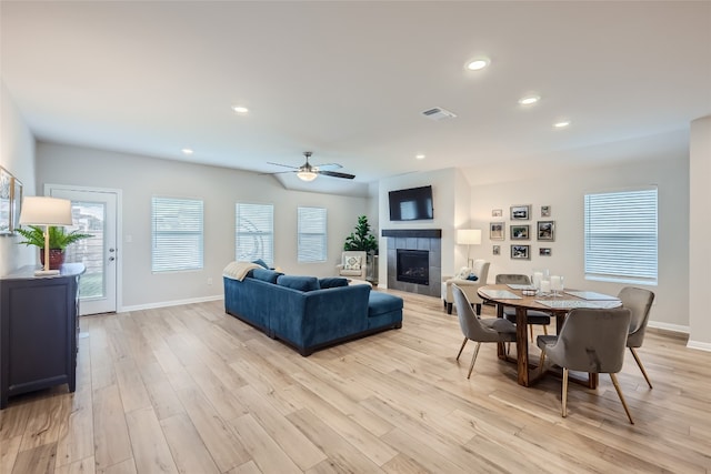 living room with a tiled fireplace, ceiling fan, and light hardwood / wood-style flooring