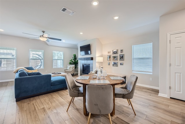 dining area featuring ceiling fan, a fireplace, and light wood-type flooring