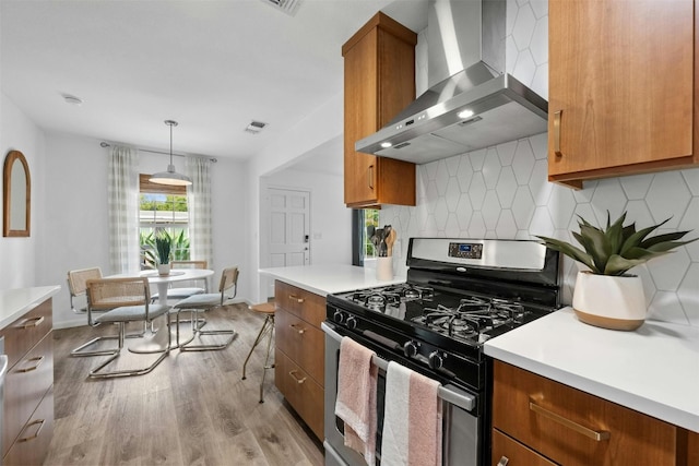 kitchen with gas range, wall chimney exhaust hood, hanging light fixtures, decorative backsplash, and light wood-type flooring