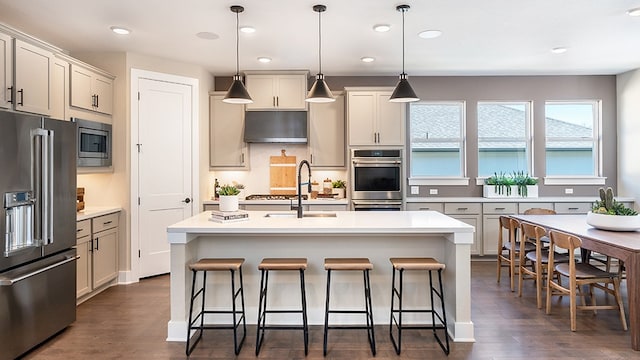 kitchen with appliances with stainless steel finishes, dark hardwood / wood-style flooring, a kitchen breakfast bar, decorative light fixtures, and a kitchen island with sink