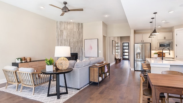 living room featuring sink, a tiled fireplace, dark hardwood / wood-style floors, and ceiling fan