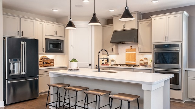 kitchen with a center island with sink, sink, hanging light fixtures, stainless steel appliances, and dark hardwood / wood-style floors