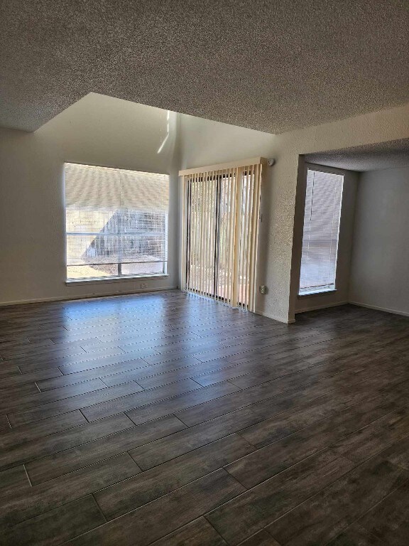 spare room featuring a textured ceiling, vaulted ceiling, and dark hardwood / wood-style floors