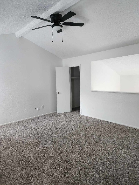 spare room with ceiling fan, lofted ceiling with beams, carpet, and a textured ceiling