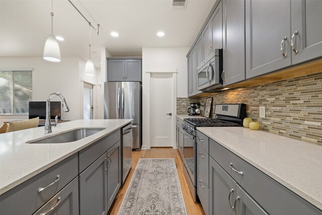 kitchen featuring gray cabinetry, sink, decorative light fixtures, light wood-type flooring, and appliances with stainless steel finishes