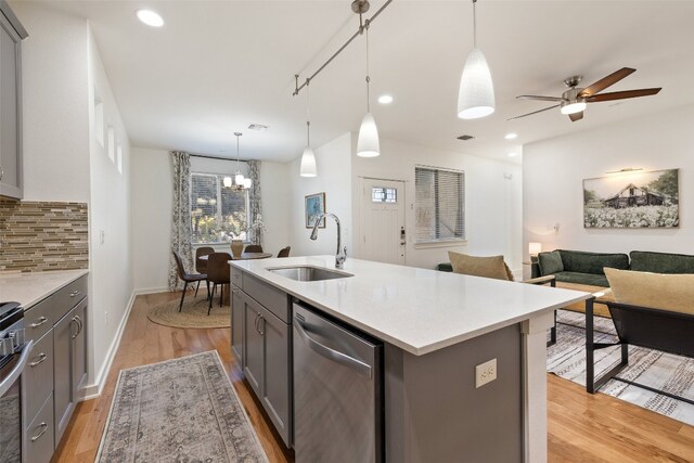 kitchen featuring sink, dishwasher, light hardwood / wood-style floors, decorative light fixtures, and a center island with sink