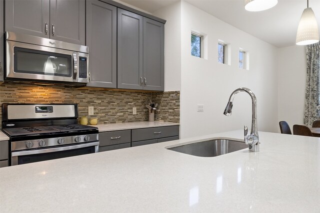 kitchen featuring decorative backsplash, gray cabinetry, sink, pendant lighting, and appliances with stainless steel finishes