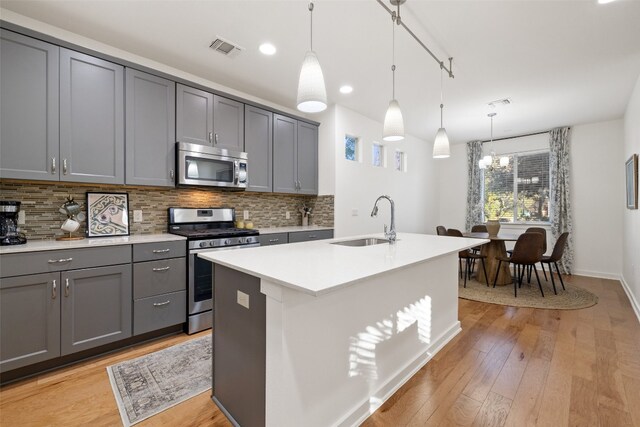 kitchen with gray cabinetry, a center island with sink, sink, pendant lighting, and appliances with stainless steel finishes