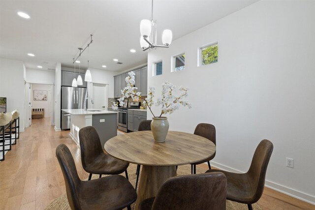 dining space featuring a notable chandelier, track lighting, sink, and light wood-type flooring