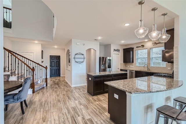 kitchen with a center island, sink, hanging light fixtures, stainless steel appliances, and light stone counters